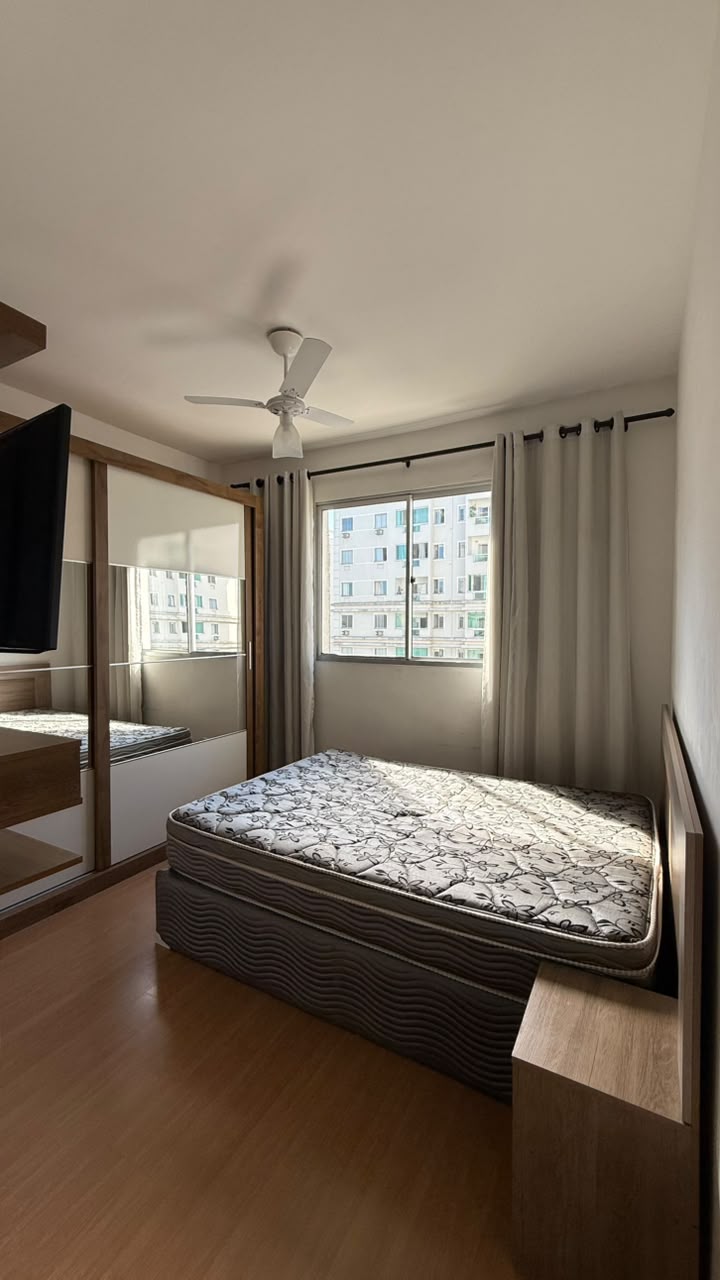 Suíte do apartamento com armário espelhado embutido, ventilador de teto e ampla janela